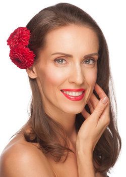Smiling middle-aged woman with red lipstick and red flowers behind ear