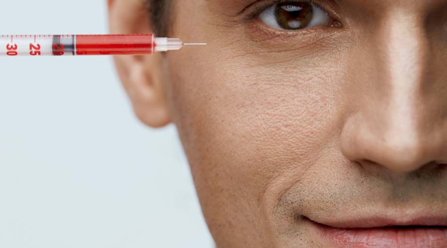 Closeup of a man holding a syringe in front of his face.